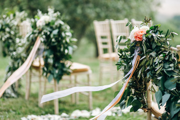 Floral garlands of green eucalyptus and pink flowers decorate wedding arch and chairs on the hill