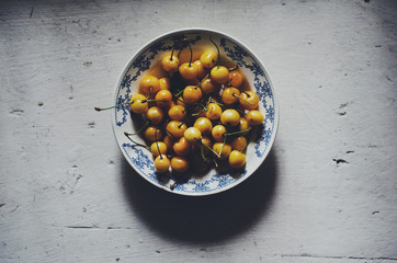 Ripe yellow cherry in blue plate on wooden vintage background