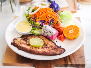 Grilled fish steak with salad with white plate on marble table.