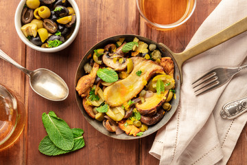 A rustic mushrooms and olives saute, shot from the top in a cast iron pan with mint and wine on a dark wooden background