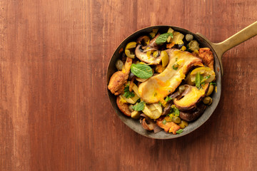 A closeup photo of a rustic mushrooms and olives saute with mint, shot from the top on a dark wooden background with a place for text