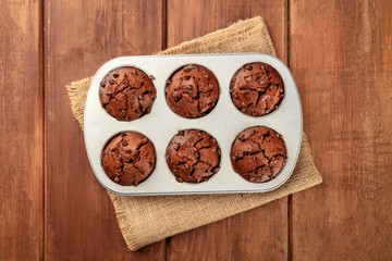 Chocolate muffins in a mould, shot from the top on a dark rustic wooden background with a place for text