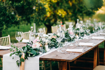 Floral garland of eucalyptus and pink flowers lies on the table for wedding reception. Italian dinner