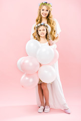 smiling child with festive air balloons standing near happy mother on pink background