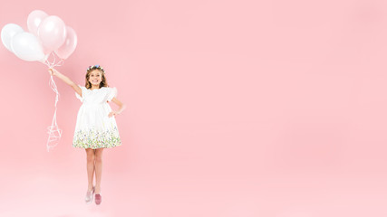 cheerful child jumping with festive air balloons on pink background with copy space