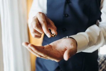 Groom holds wedding ring standing before the window in a hotel room