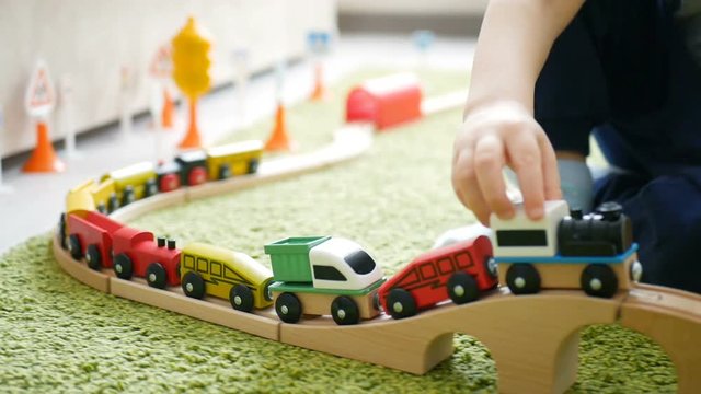 Two years old boy plays with wooden railroad in a sunny room