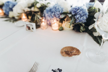 Fototapeta na wymiar Wedding table decoration. Floral garland of greenery and blue flowers lies between glasses on the white table