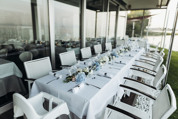 Wedding table decoration. Floral garland of greenery and blue flowers lies between glasses on the white table