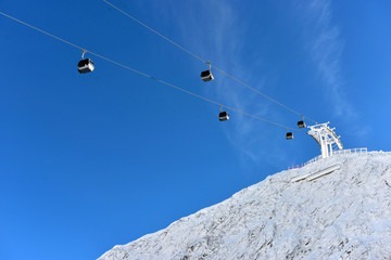 Ski resort with cable cars or aerial lift and ski-lift moving above the ground against winter landscape with mountains