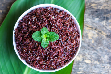 cooked purple rice berry in bowl over green leaf background on wooden table closeup, healthy eating food concept 
