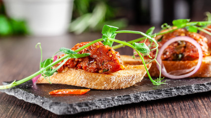 The concept of Mexican cuisine. Beef tartare with parsley, French mustard beans on baguette croutons. A dish in the restaurant on a black stone slate. Background image. copy space