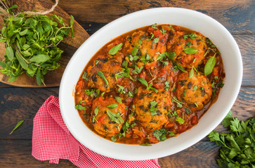 Chopped fish cutlets in spicy tomato sauce with fresh mint. White dish on wooden rustic table, top view