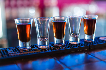 Several shots of different drinks at a party in a nightclub.  drink shots in blue and warm light in bar. 