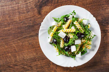 pasta fusilli salad with arugula, cheese and olive in white plate on a wooden background