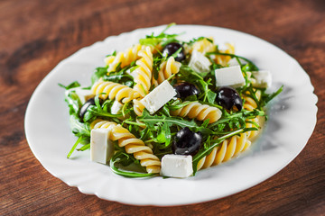 pasta fusilli salad with arugula, cheese and olive in white plate on a wooden background