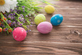 Colorful Easter eggs and spring flowers on rustic wooden background.