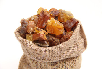 Natural raw amber stone in jute bag isolated on white background. Multiple amber gemstone in various shapes and colour gathered in bag. Jewelry components.