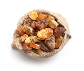 Natural raw amber stone in jute bag isolated on white background. Multiple amber gemstone in various shapes and colour gathered in bag. Jewelry components.