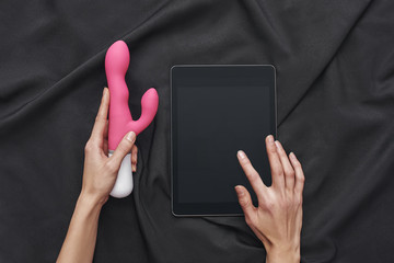 How to Use a Vibrator? Top view of female hands holding pink vibrator and digital tablet against of...