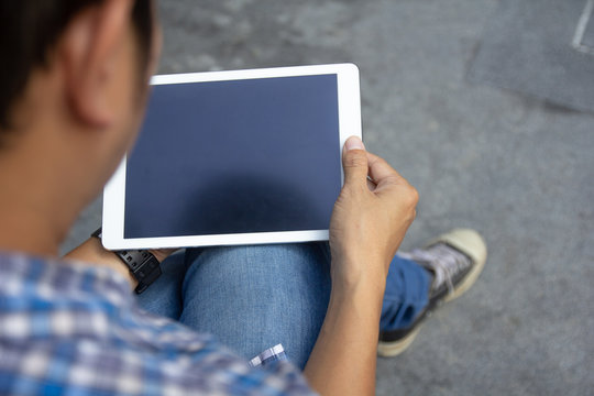 Top view mockup image of man hands holding and using white digital tablet pc with black blank desktop screen in hands while sitting on the floor, top view. Online internet