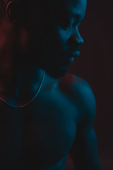 Red and blue lighted portrait of young and sexy muscular shirtless man with neck chain. Flat shadows