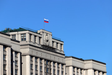 Fototapeta na wymiar Russian flag on the Parliament building in Moscow against blue sky. Facade of State Duma of Russia with soviet coat of arms, russian authority