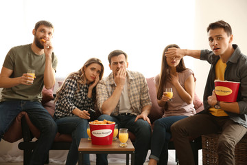 Group of friends eating nuggets while watching horror movie on TV at home