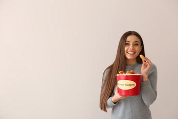 Young woman with bucket of tasty nuggets on light background