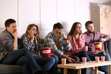 Group of friends eating nuggets while watching horror movie on TV at home