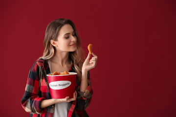 Beautiful woman with bucket of tasty nuggets on color background