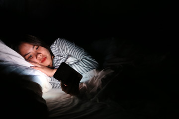 Asian woman using smartphone at night on the bed in dark room, Using smartphone in dark may be causes of eye pain symptom,Health Concept