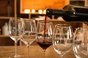 Pouring of tasty red wine into glasses on table