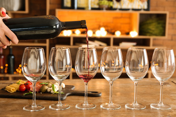 Pouring of tasty red wine into glasses on table