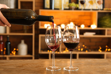 Pouring of tasty red wine into glasses on table