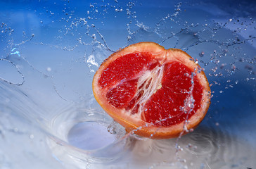 Ripe cut grapefruit with water splash on color background