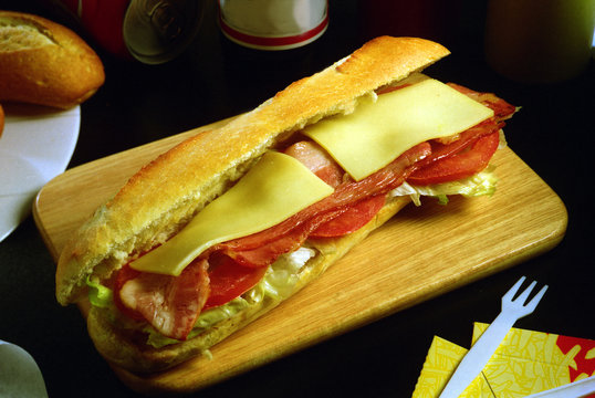 Un bocadillo con una barrita de pan, lechuga, tomate, beicon y queso.