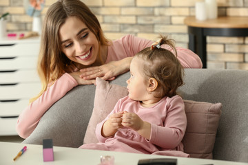Young woman with her cute little daughter playing with cosmetics at home