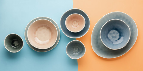 Beautiful blue, grey, beige dinnerware, plates bowls on blue pastel orange background table, top view, selective focus