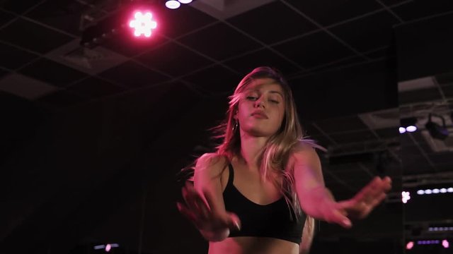 Blondy girl sexy moving her ass, dancing twerk in studio. Sexy blonde shaking booty dancing twerk. Young girl dancing in dark, dancing studio in white shirts and black bra. Slow motion. Low angle view