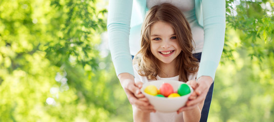easter, holidays and people concept - happy smiling girl with mother with colored eggs over green natural background