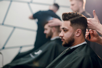 Young handsome brunette man getting haircut by hairdresser in barbershop.