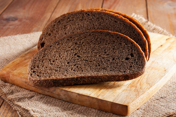 Dark rye bread on wooden board on burlap.