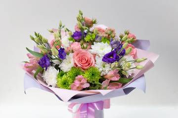An impressive bouquet of fresh flowers (Main colors: white, pink, green, purple) in a paper package in a vase on a light background.