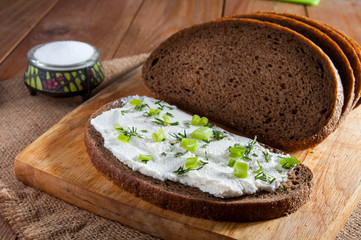 Dark rye bread, sandwich with cream on wooden cutting board and salt in saltshaker on burlap.