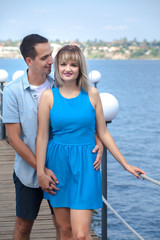 young couple, a guy and a girl are standing on a pier near a river, happy, hugging. Walk on a summer sunny day. Love, feelings