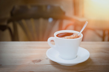 Cup of espresso coffee on a wooden table against a sun flare light. Empty copy space for Editor's text.