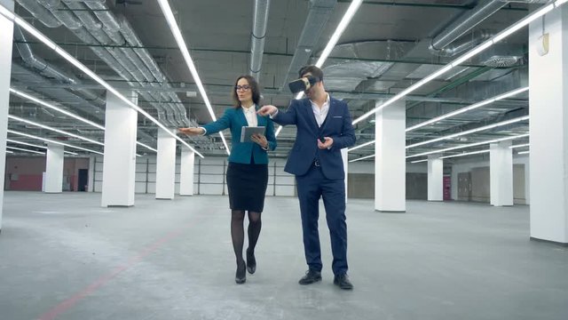 Female agent is showing empty office premises to a man in VR-glasses