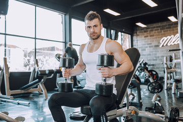 Athletic man doing exercises with dumbbells in gym