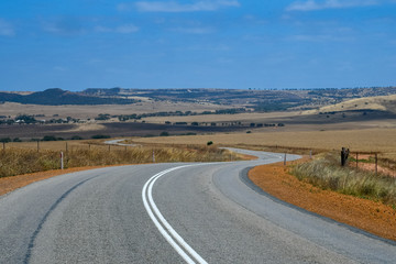 Fototapeta na wymiar Australian bush road curving through dry landscape with yellow farmland